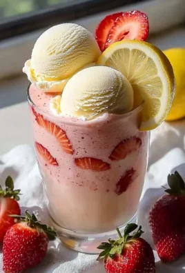 Strawberry frosted lemonade in a glass, garnished with fresh strawberries and lemon slices.