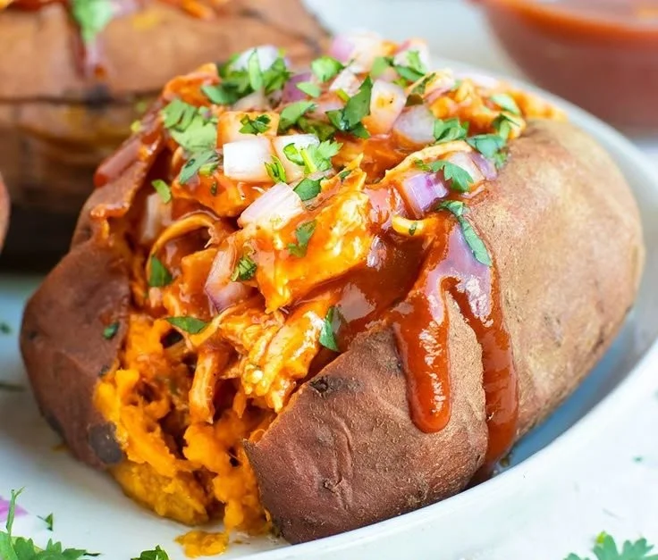 BBQ chicken stuffed sweet potatoes with toppings on a wooden table