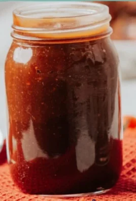 Homemade hickory BBQ sauce in a jar with ingredients on a wooden table.