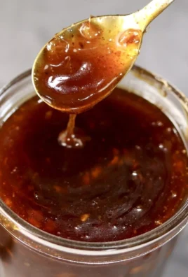 Homemade peach BBQ sauce in a jar with fresh peaches and herbs