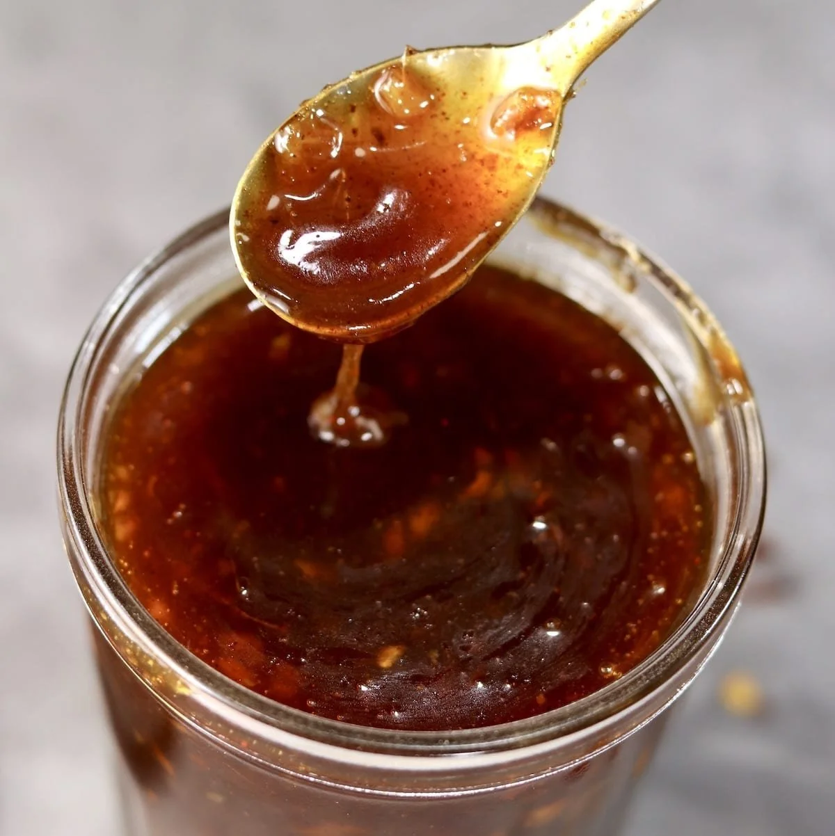 Homemade peach BBQ sauce in a jar with fresh peaches and herbs