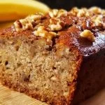Ultimate Banana Nut Bread loaf with walnuts and bananas on a wooden table
