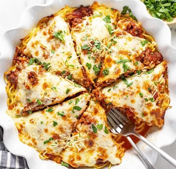 Delicious cheesy spaghetti pie served on a plate with herbs