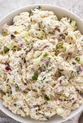 Delicious chicken salad served on a white plate with fresh vegetables.