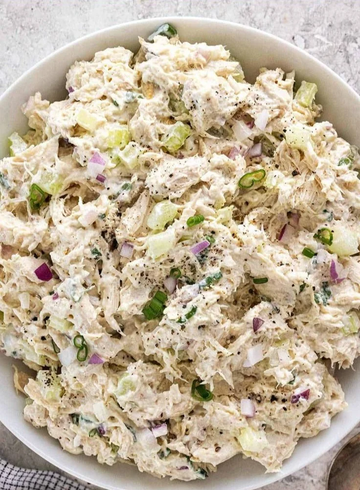 Delicious chicken salad served on a white plate with fresh vegetables.