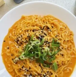Bowl of homemade Buldak Carbonara Noodles garnished with herbs