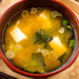 Bowl of homemade miso soup with tofu and green onions served with chopsticks.