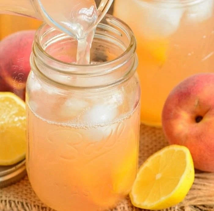Refreshing homemade peach lemonade in a glass with fresh peaches and lemons