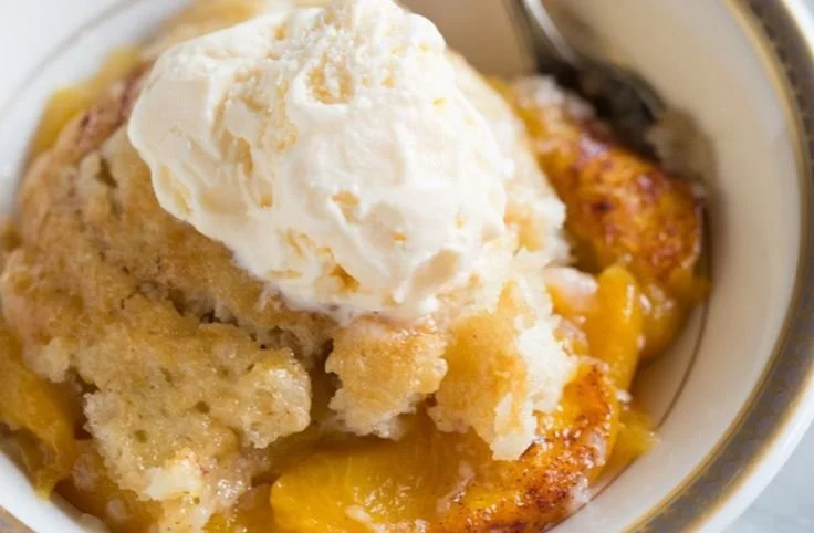 Slice of old fashioned peach cobbler with golden crust and fresh peaches